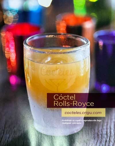 Cóctel Rolls-Royce con brandy, jugo de naranja y triple seco en vaso de vidrio sobre barra con fondo desenfocado.