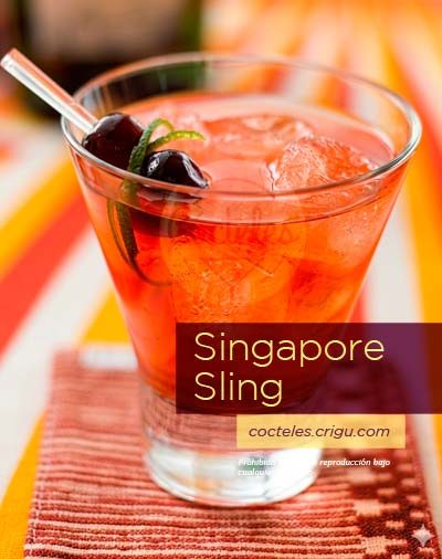 Cóctel Singapore Sling con ginebra, de color rojizo, aguardiente de cereza y decoración de cerezas marrasquino, presentado en vaso con hielo sobre fondo de mantel a rayas naranjas y blancas.
